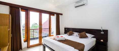 Ein Hotelzimmer mit einem großen Bett, einem Holzschrank, einem Nachttisch und Blick ins Freie.