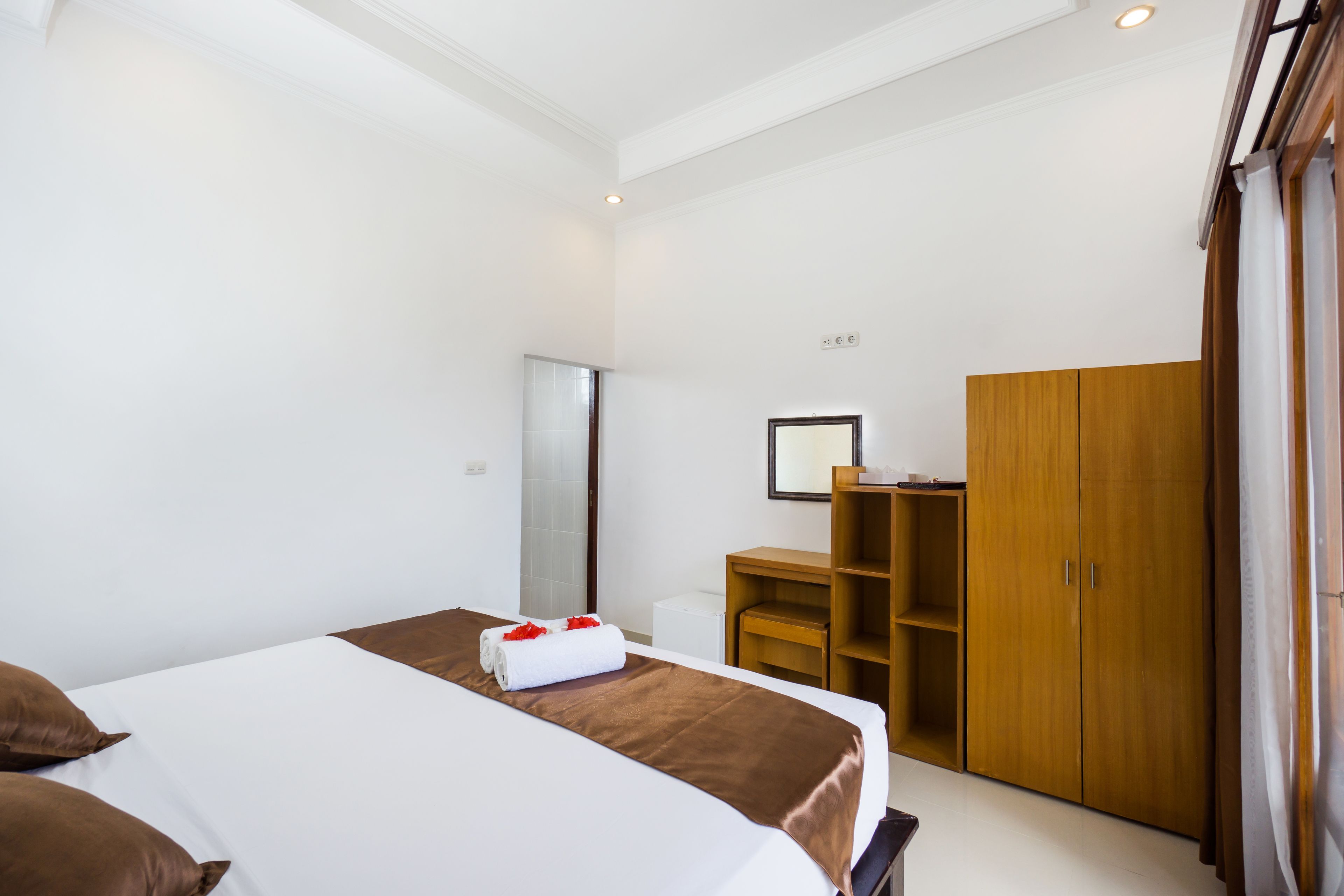 A hotel room with a large bed, a wooden wardrobe, a desk, and a mirror on the wall.