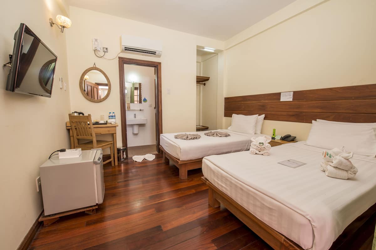 A hotel room with two beds, a desk, a TV, and a bathroom visible through an open door.