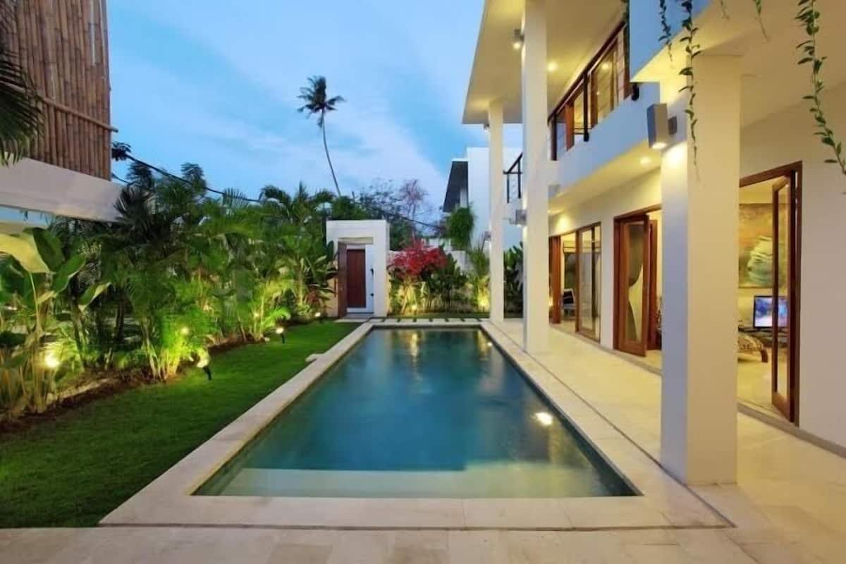 A modern building with a swimming pool, surrounded by lush greenery and palm trees.