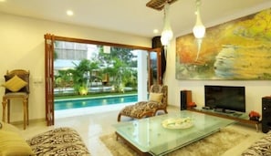 A living room with a glass coffee table, a sofa, a TV, and a painting. - Moonlight Bali (Nusa Dua)