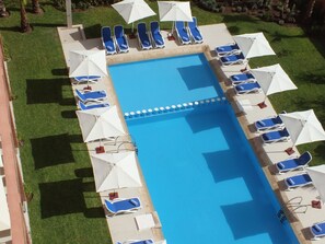 Una piscina al aire libre, sombrillas, sillones reclinables de piscina