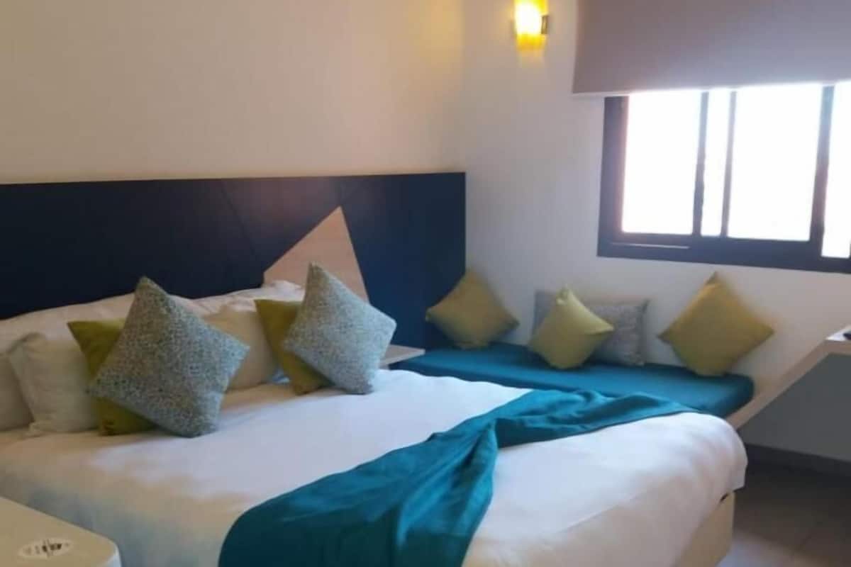 A hotel room with a large bed, multiple pillows, a bedside table, and a window with blinds.