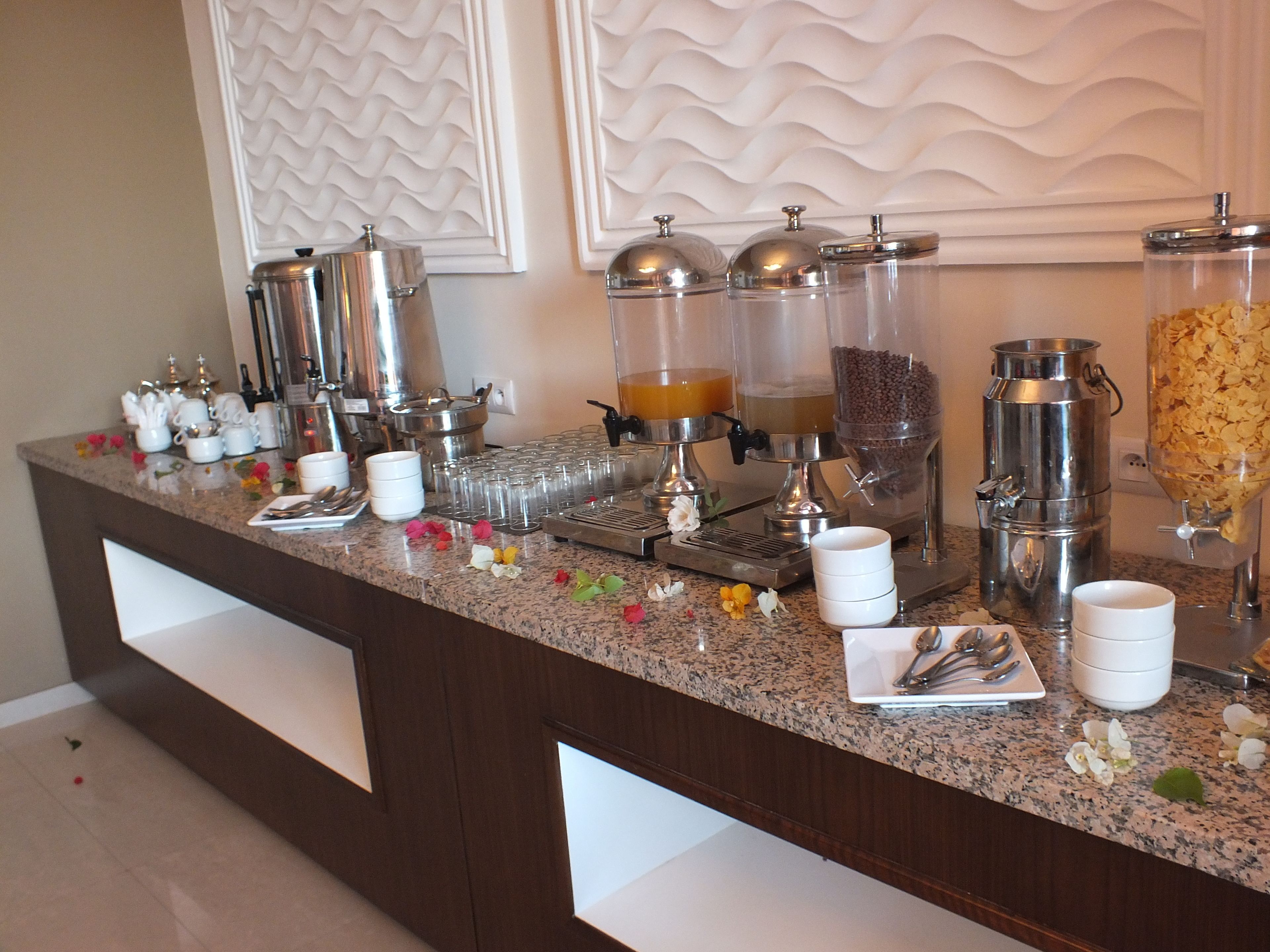 A buffet setup with various food and drink dispensers, including a cereal dispenser and a coffee machine.