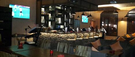 A bar area with a counter, seating, and a television screen.