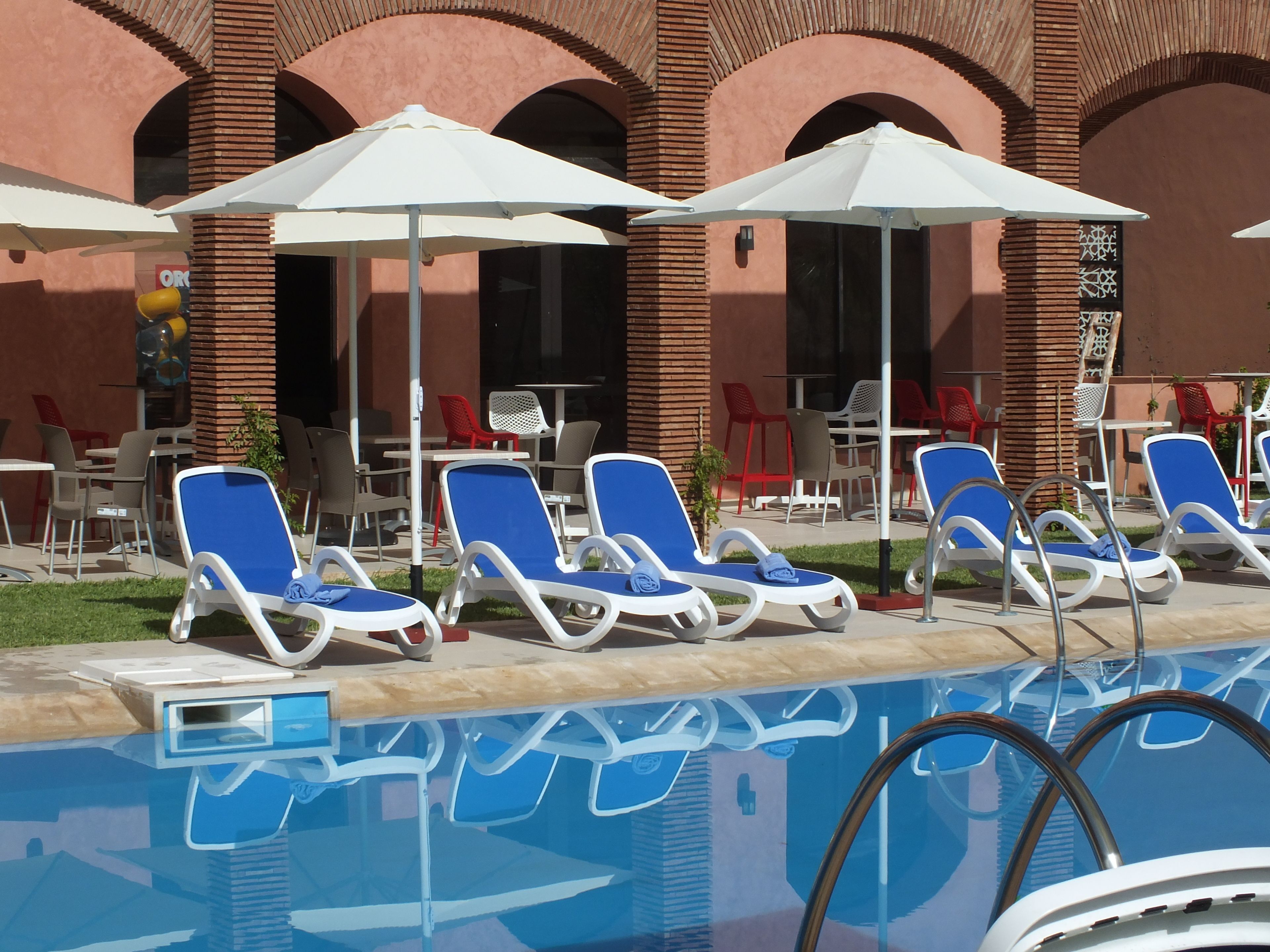 Zona de piscina amb gandules i ombrelles, envoltada d'un edifici amb finestres d'arc i façana de maó.