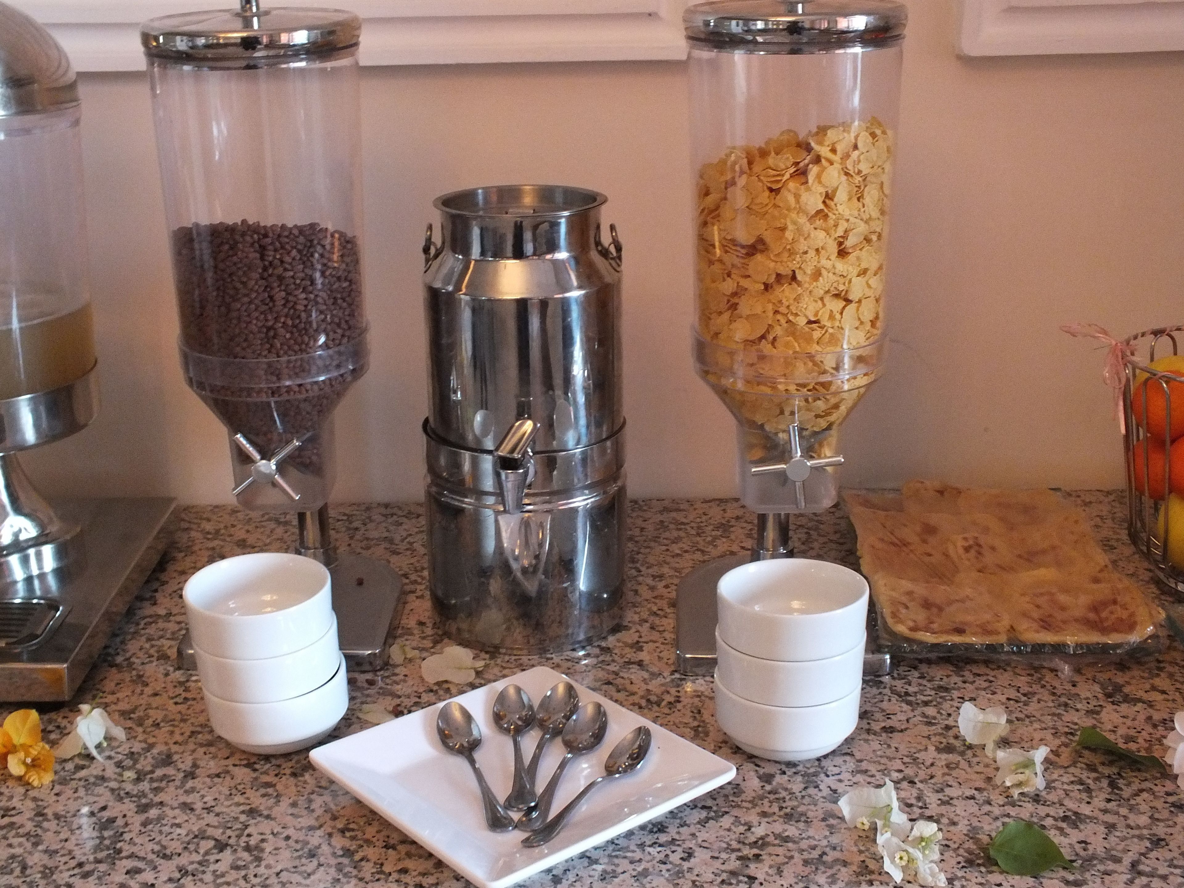Una encimera de cocina con tres dispensadores de alimentos, dos tazas blancas, un plato con cucharas y un pastel a la derecha.