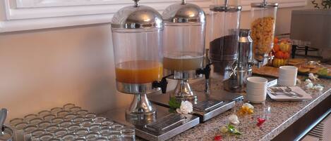 A buffet setup with multiple beverage dispensers, a fruit display, and a variety of dishes.