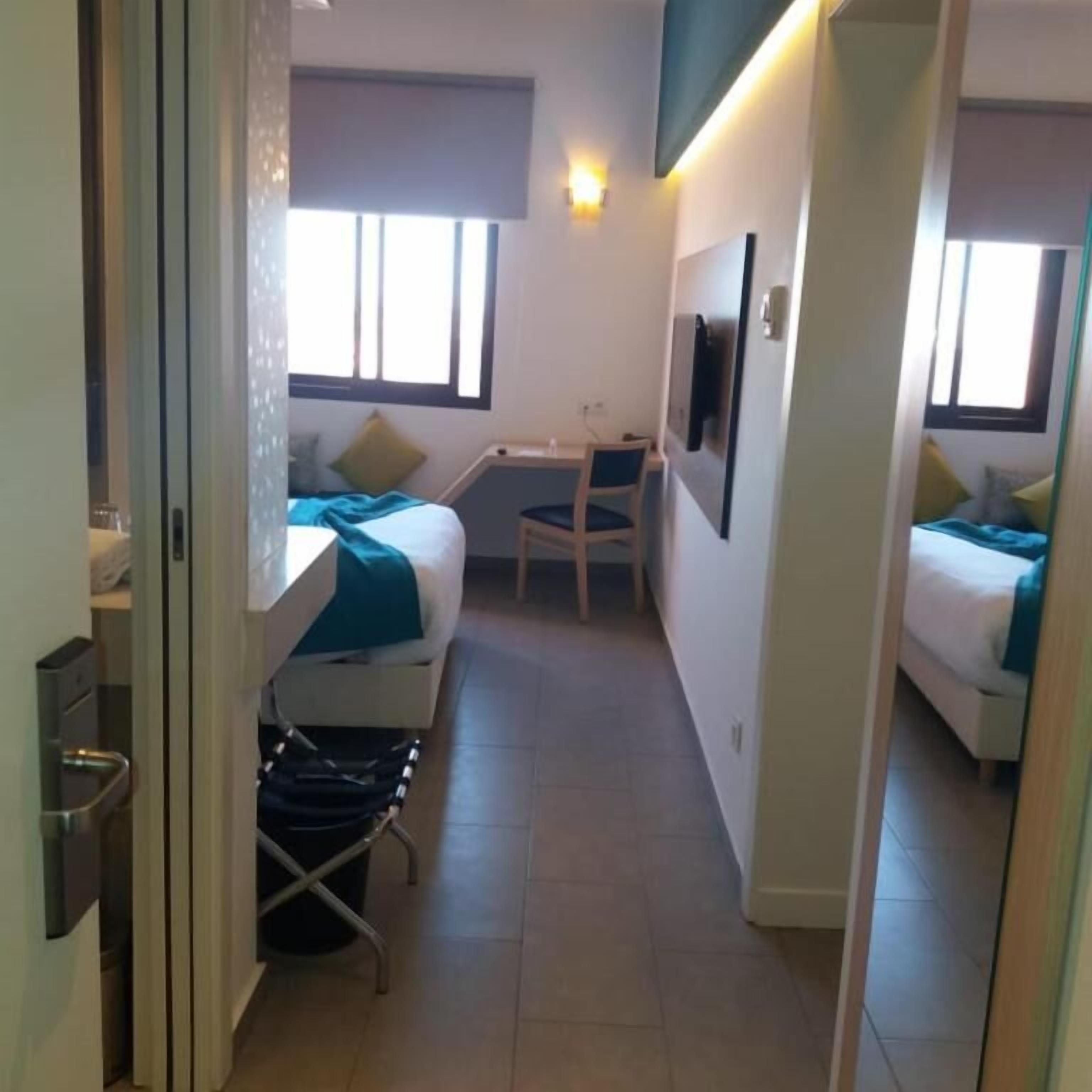 A compact hotel room with two beds, a desk, and a chair.