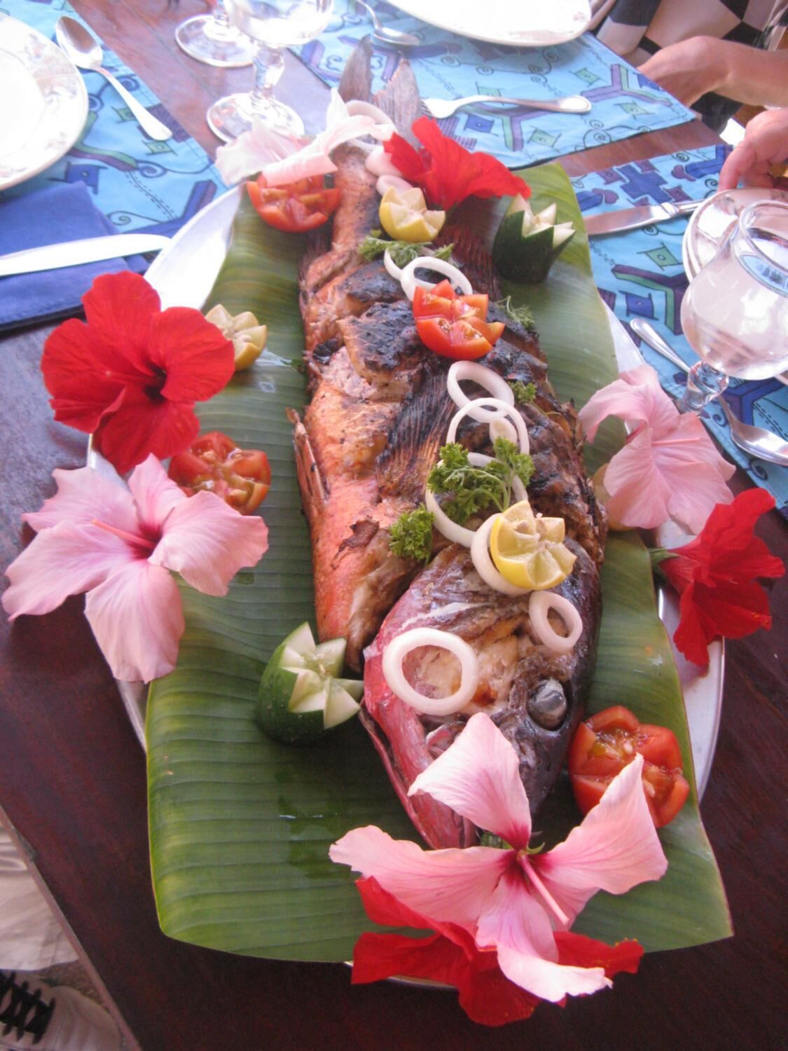 A fish dish with vegetables and flowers on a banana leaf.