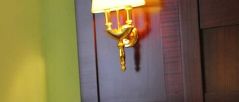 A hotel room with a bed, a wall-mounted lamp, and a heart-shaped towel arrangement on the bed.