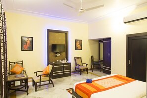 A hotel room with a bed, two chairs, a desk, a wardrobe, and a television. - OYO 1152 Sodala (Jaipur)