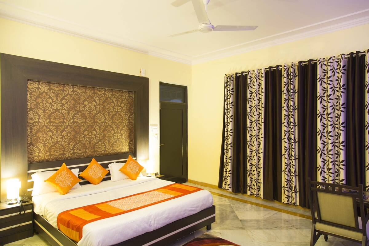 Una habitación de hotel con una cama grande, un cabecero con diseño estampado, un ventilador de techo y cortinas con motivos de hojas.