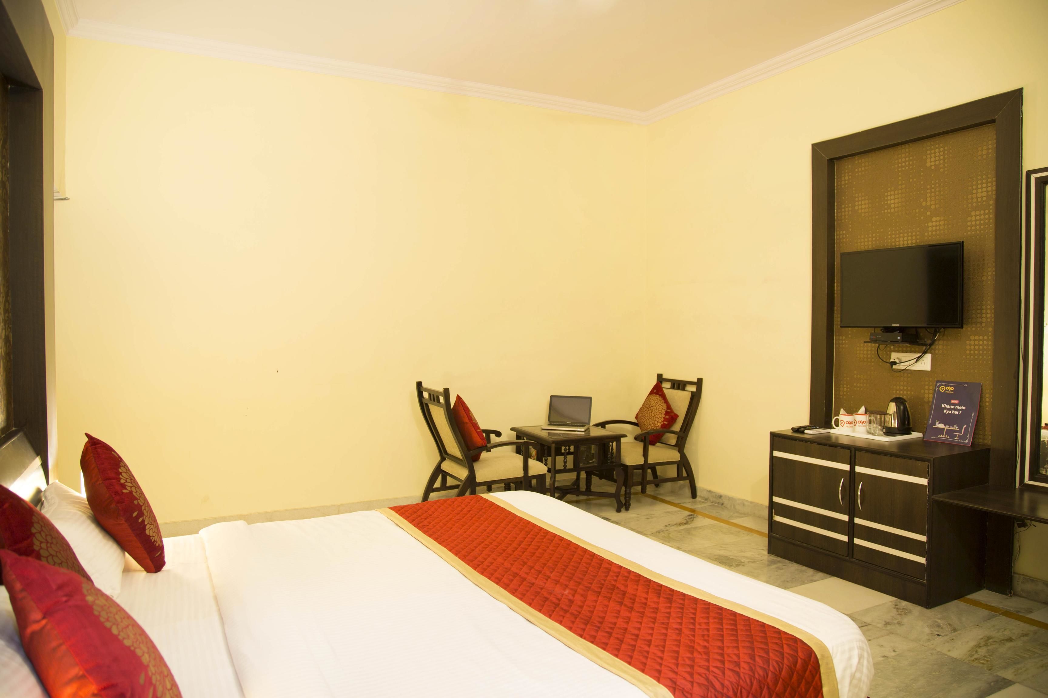 Habitación de hotel con cama, escritorio con computadora portátil, dos sillas, televisor y minibar.