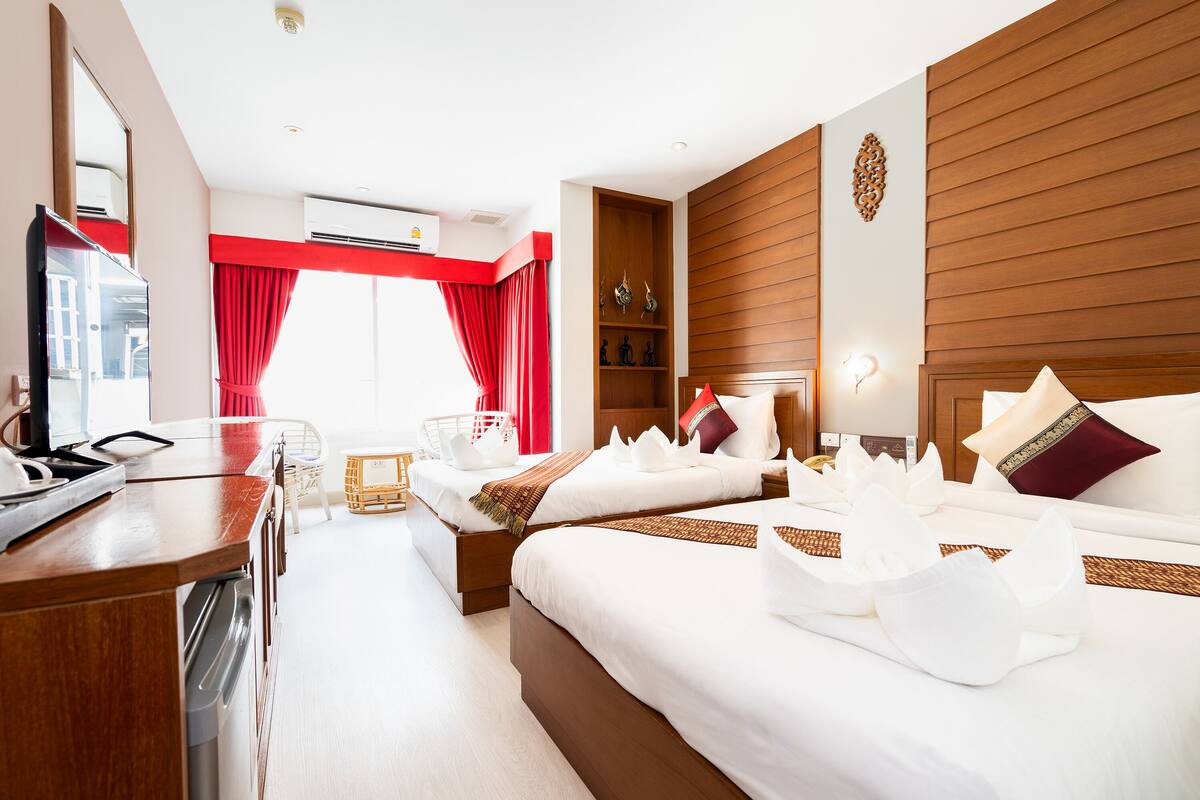 Habitación de hotel con dos camas, cabecero de madera, cortina roja, estante de madera con adornos y escritorio con televisor de pantalla plana.
