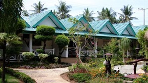 A pathway leading to a building with a green roof, surrounded by well-maintained gardens and palm trees.