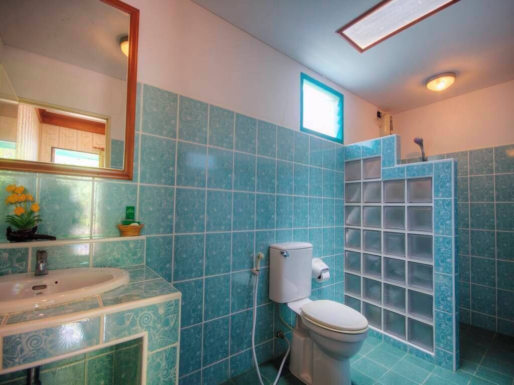 A bathroom with blue tiles, a white sink, a toilet, and a shower enclosure.