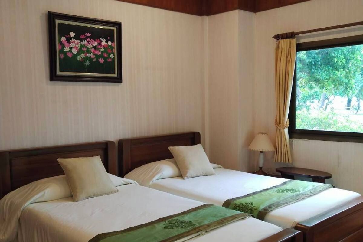 Cama de casal com colcha verde, cabeceira de madeira e janela com cortinas.