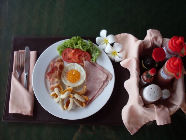 Un plato con un huevo cocido, jamón, tomates, lechuga y fideos, acompañado de salsas y una servilleta sobre una mesa.