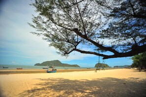 Una playa con barcos, un árbol grande y islas a lo lejos.