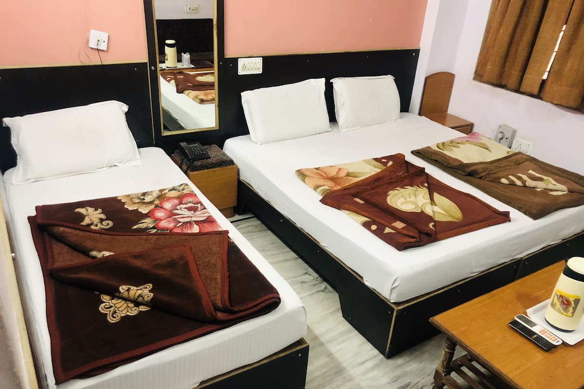 A hotel room with two beds, each with a different patterned blanket, a wooden nightstand with a remote control, and a mirror reflecting the room.