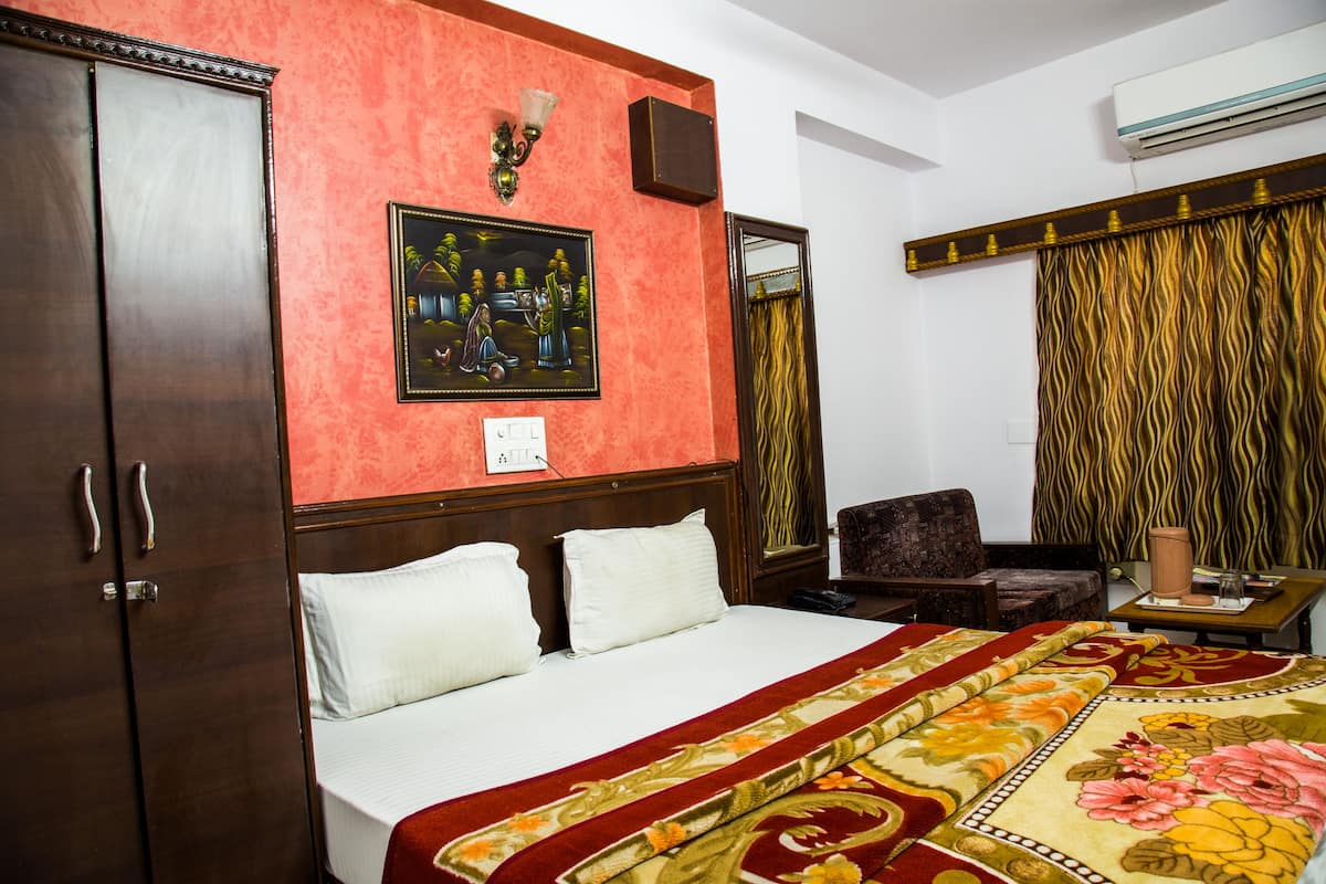 A hotel room with a large bed, a wardrobe, a painting on the wall, a chair, and a curtain.