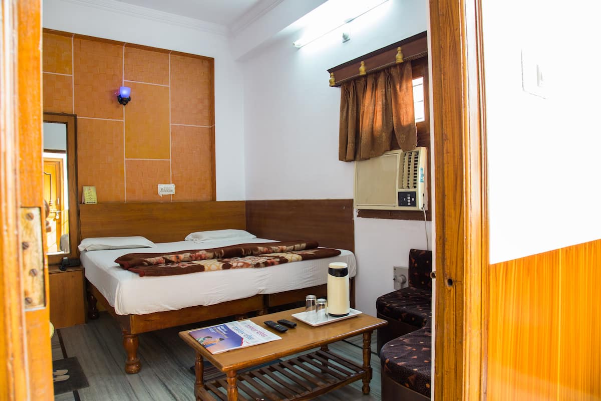A hotel room with a wooden bed, a bedside table with a remote control, a pillow, and a blanket.