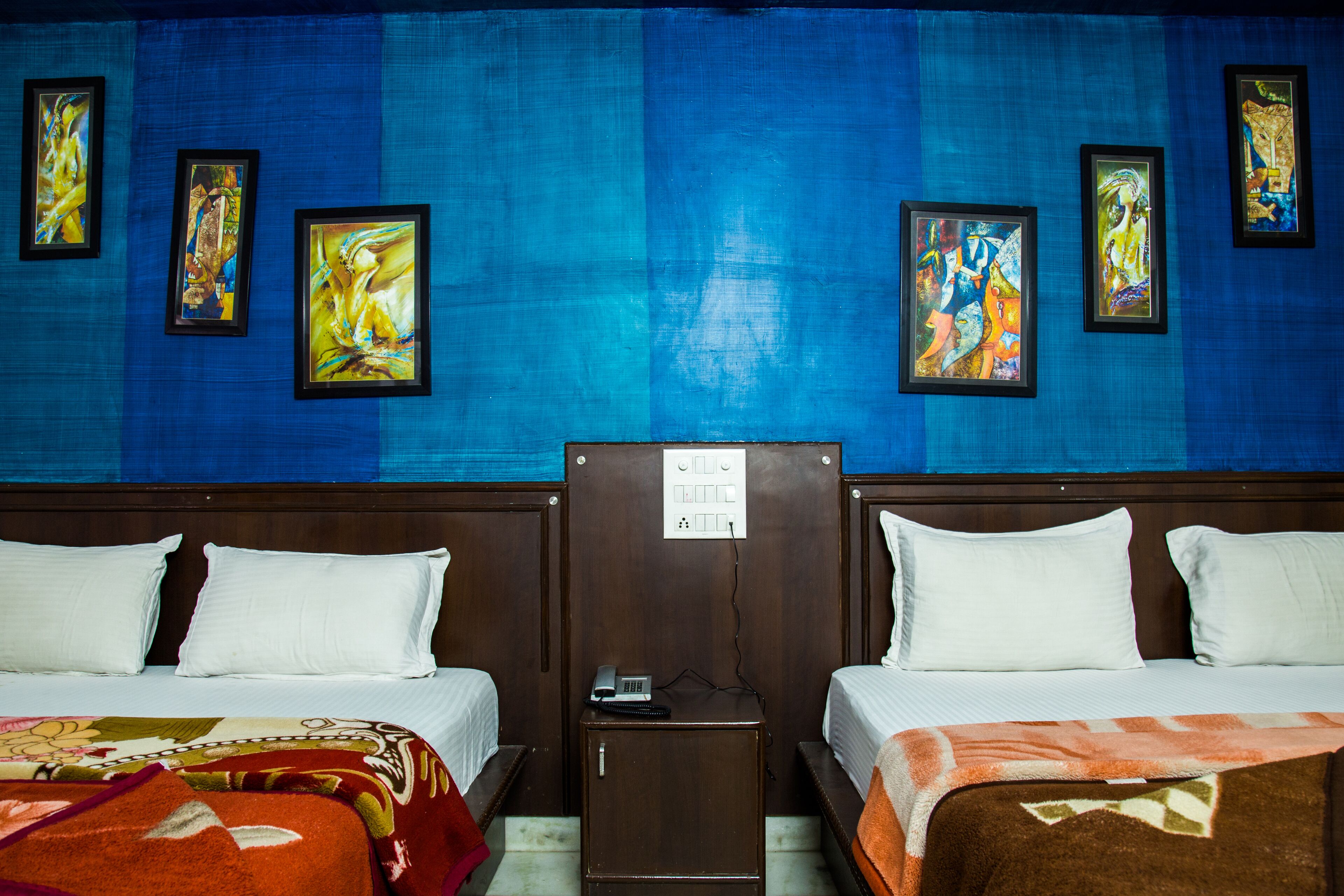 Een hotelkamer met twee bedden, een nachtkastje en een muur met ingelijste kunstwerken.