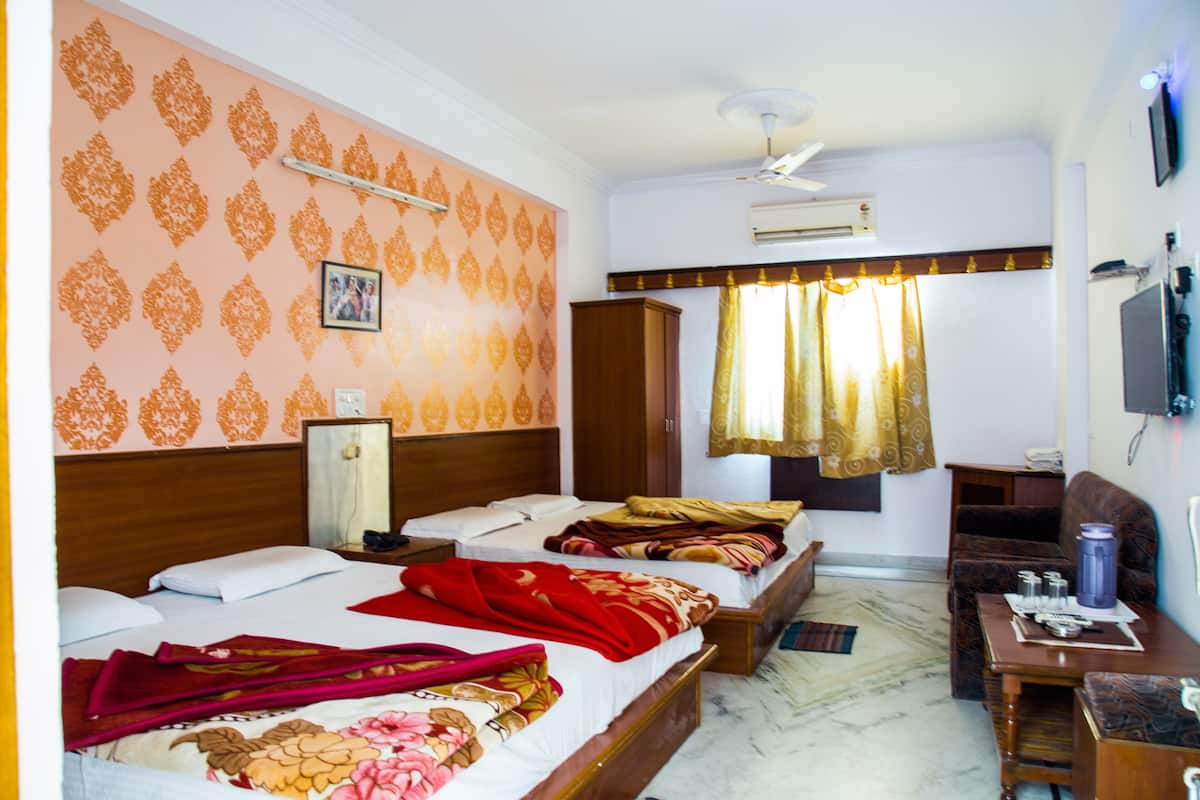 A hotel room with two beds, a sofa, a TV, and a ceiling fan.