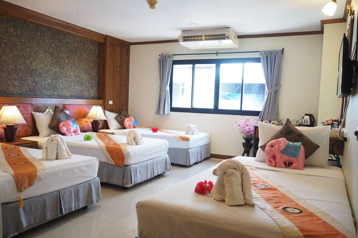 A hotel room with two beds, a small table, a window with curtains, and a ceiling fan.