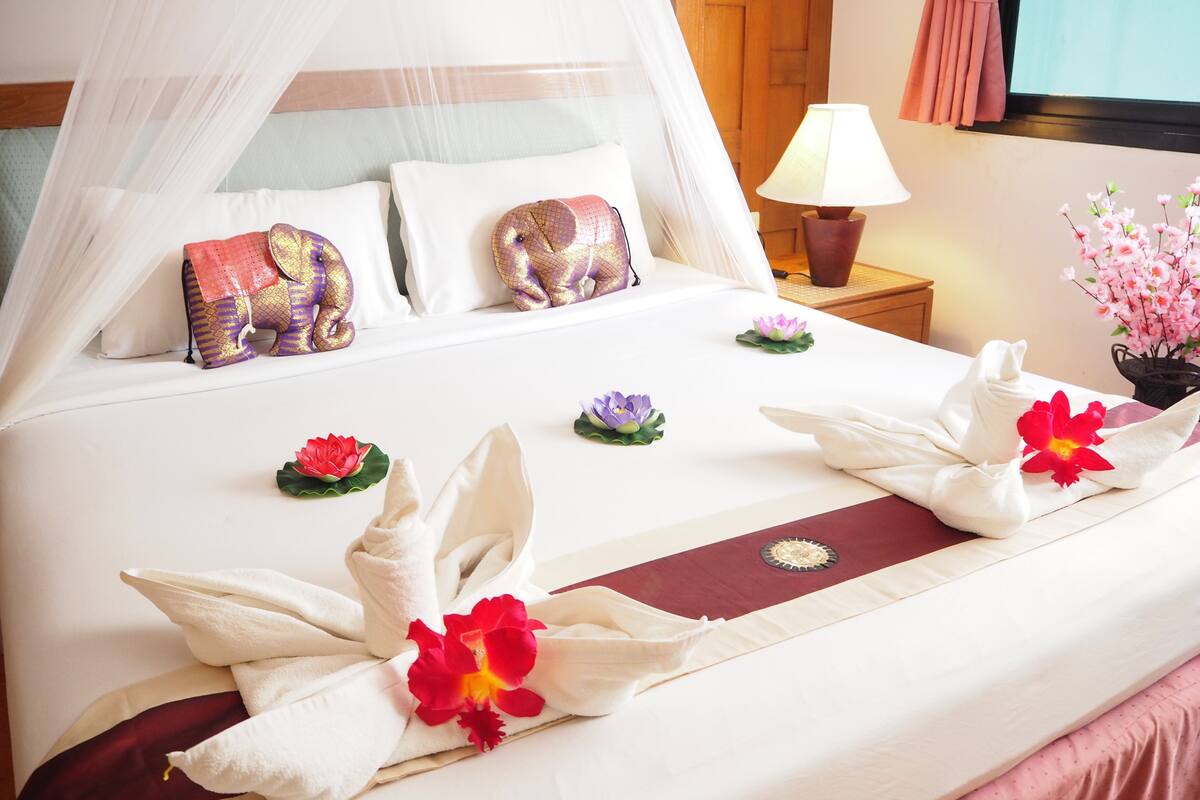 A neatly made bed with white linens, decorative pillows, and floral arrangements.