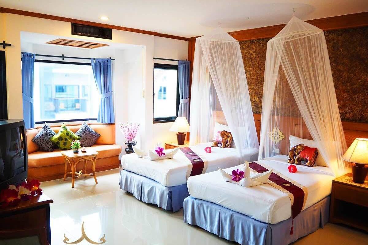 A hotel room with two beds, a sofa, a TV, and a window with curtains.