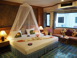 A hotel room with a bed, a nightstand, a bedside table, a window, and a view of the outside. - Your Place Inn (Karon)