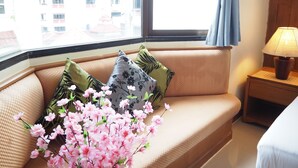 A hotel room with a sofa near a window, a lamp on a bedside table, and a vase with flowers. - Your Place Inn (Karon)