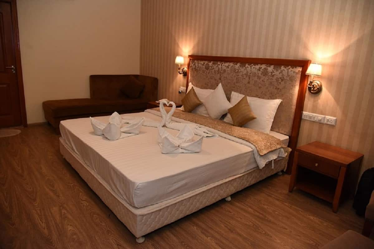 Habitación de hotel con una cama grande, cabecera de madera, dos lámparas de noche y una mesita de noche pequeña de madera.