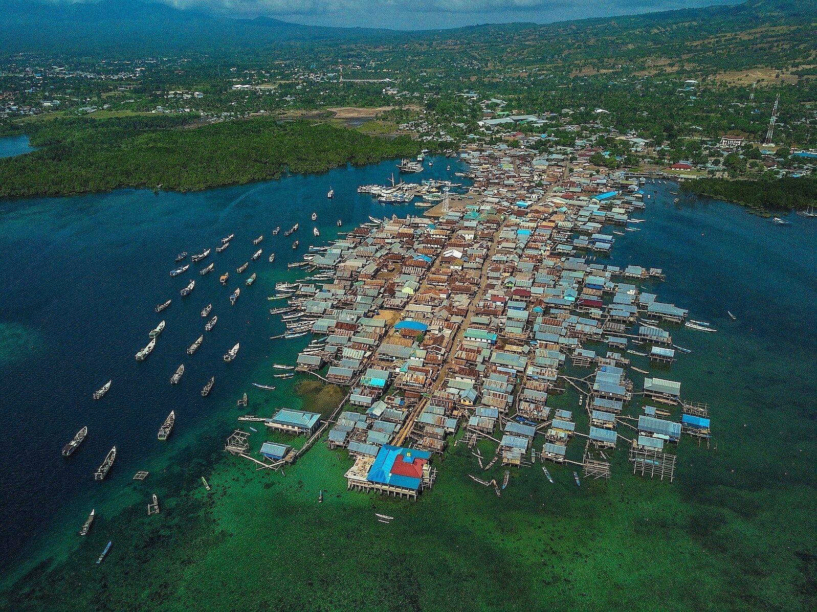 Vista aérea de un asentamiento costero con numerosos barcos amarrados a lo largo de la orilla y un denso conjunto de edificios pequeños y adosados.