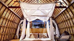 Een bed met hemelbed in een kamer met rieten dak.