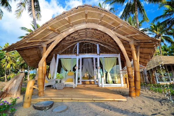 A bamboo structure with a covered entrance and a sandy foreground.