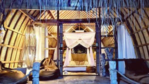 Een rieten dakconstructie met een bed, kussens en een baldakijn.