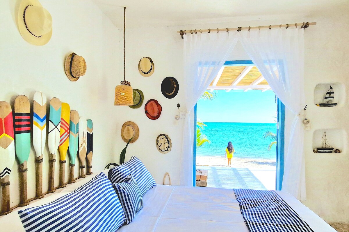 Une chambre avec un lit, une vue sur la plage et différents chapeaux accrochés au mur.