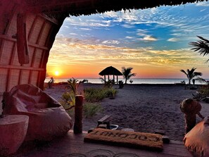 Une vue sur la plage avec une structure à toit de chaume, des palmiers et un coucher de soleil.