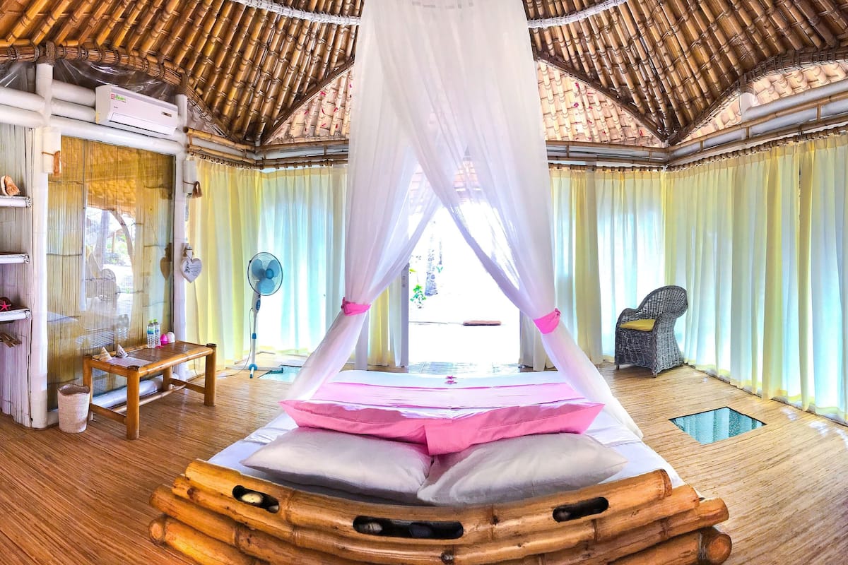 Une chambre avec un lit en bambou, un ventilateur et une chaise.