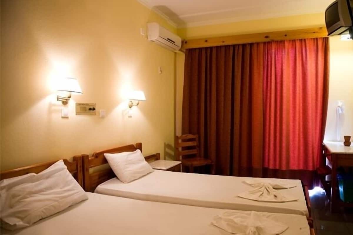 Ein Hotelzimmer mit zwei Einzelbetten, einem Holzkopfstück, einem Sessel, einem kleinen Tisch und einem Fernseher.
