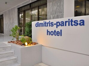 A sign for Dimitris-Paritsa Hotel with a modern design and a stone planter with plants.