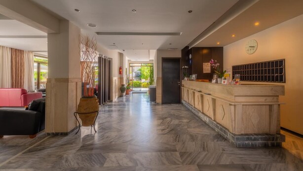 A hotel lobby with a reception desk, a seating area with a red sofa, and a hallway leading to the exit. - Dimitris Paritsa Hotel (Kos)