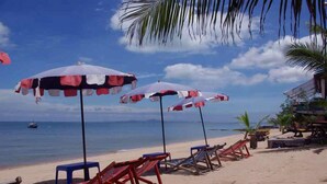 A beach with umbrellas and chairs, a boat in the water, and a building in the background. - Sea Falcon Hotel (Sattahip)