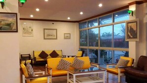 A cozy living room with yellow sofas and armchairs, a coffee table, and large windows offering a view of the outdoors. - Sea Falcon Hotel (Sattahip)