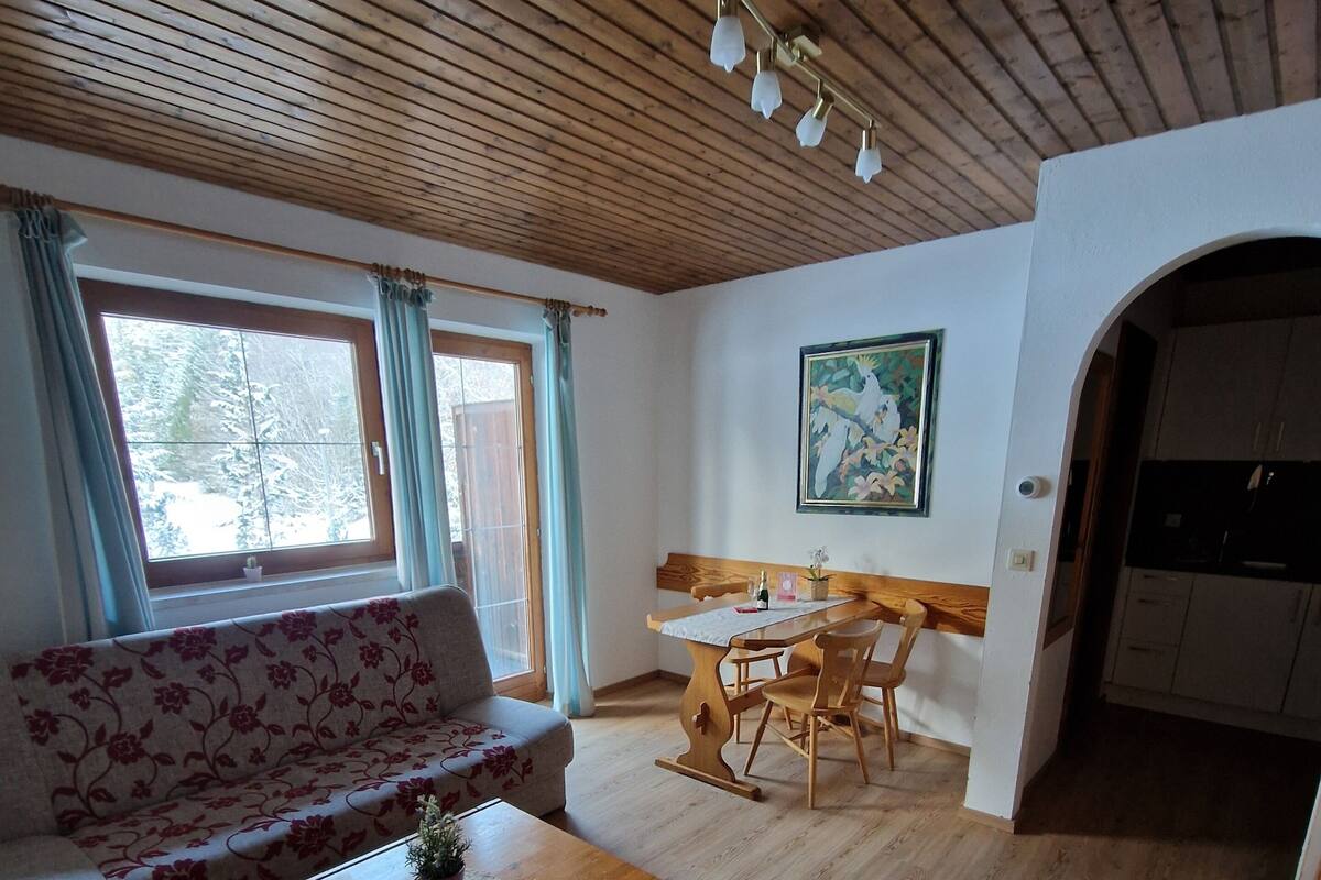 Un vaste espace de vie doté d’un plafond en bois, d’un canapé, d’une table à manger avec des chaises, et d’un coin cuisine visible à travers une arche.