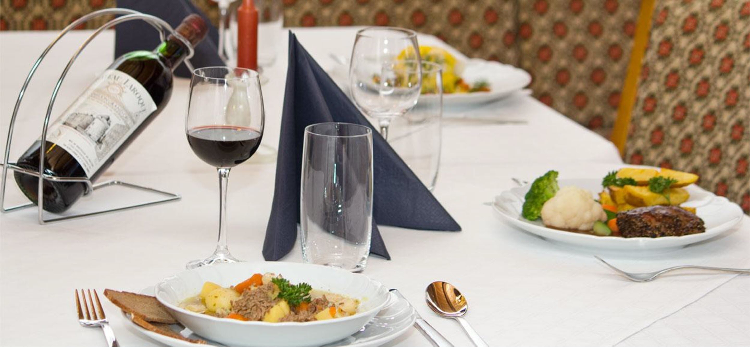 Una mesa de comedor con platos de comida, copas de vino y una botella.