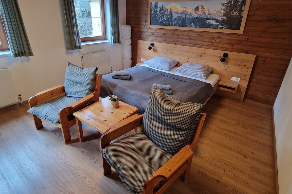 Une pièce de cabane en bois comprenant un lit, deux chaises, une table et un tableau accroché au mur.